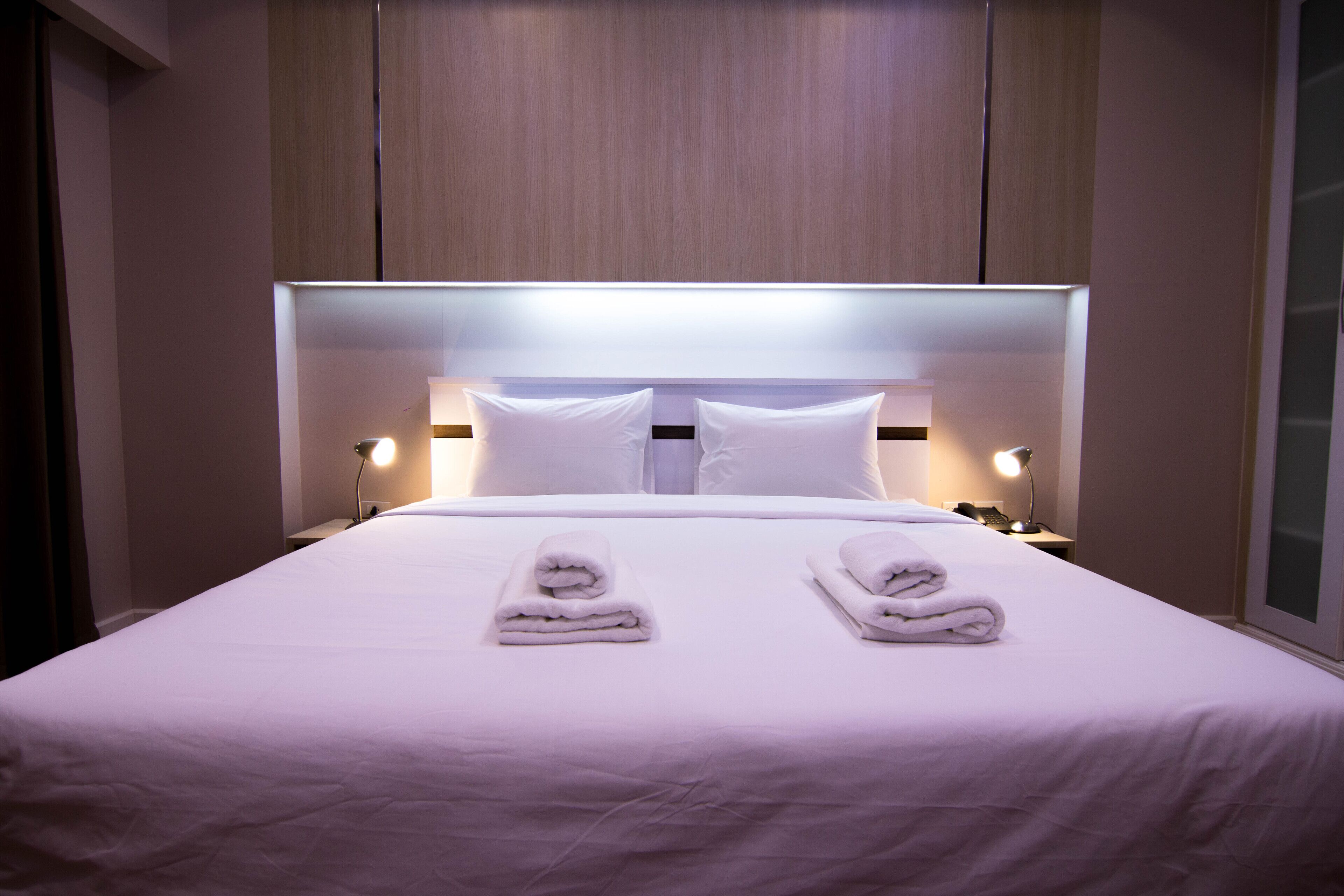 Quarto de hotel com uma cama grande, duas almofadas, duas luminárias de cabeceira e duas toalhas dobradas na cama.