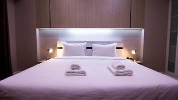 Quarto de hotel com uma cama grande, duas almofadas, duas luminárias de cabeceira e duas toalhas dobradas na cama.