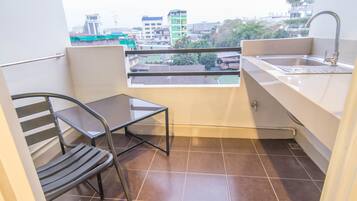 A small balcony with a metal chair, a small table, a sink, and a view of the cityscape.