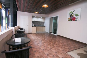 A spacious balcony with a tiled floor, a dining area with a table and chairs, and a kitchen in the background. - At Home at Udon (Udon Thani)
