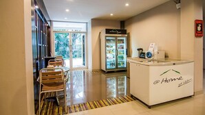 Un hall de hotel con mostrador de recepción, un refrigerador con bebidas y un área de descanso con sillas.