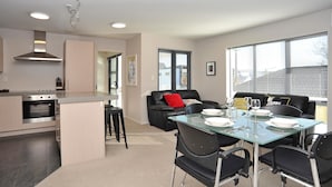 A modern kitchen with a built-in stove, a dining area with a glass table and black chairs, and a black leather sofa with a red pillow. - Carlton Villa 3 (Christchurch)
