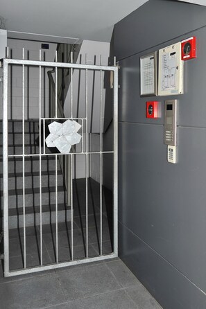 A metal gate with a keypad and emergency buttons, a staircase, and a wall-mounted control panel.
