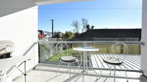 A balcony with a table and two chairs, a grill, and a view of a building and trees. - Carlton Villa 3 (Christchurch)