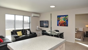 A modern living room with a black leather sofa, a glass dining table, and a kitchen area with a granite countertop. - Carlton Villa 3 (Christchurch)