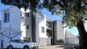 A modern two-story building with a white facade, a car parked in front, and a tree to the right. - Carlton Villa 3 (Christchurch)