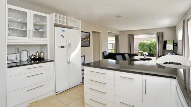 Una cocina moderna con armarios blancos, encimera negra y zona de comedor con mesa y sillas.