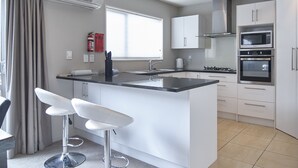 Una cocina moderna con una isla central, armarios blancos, electrodomésticos de acero inoxidable y un ventanal con persianas.