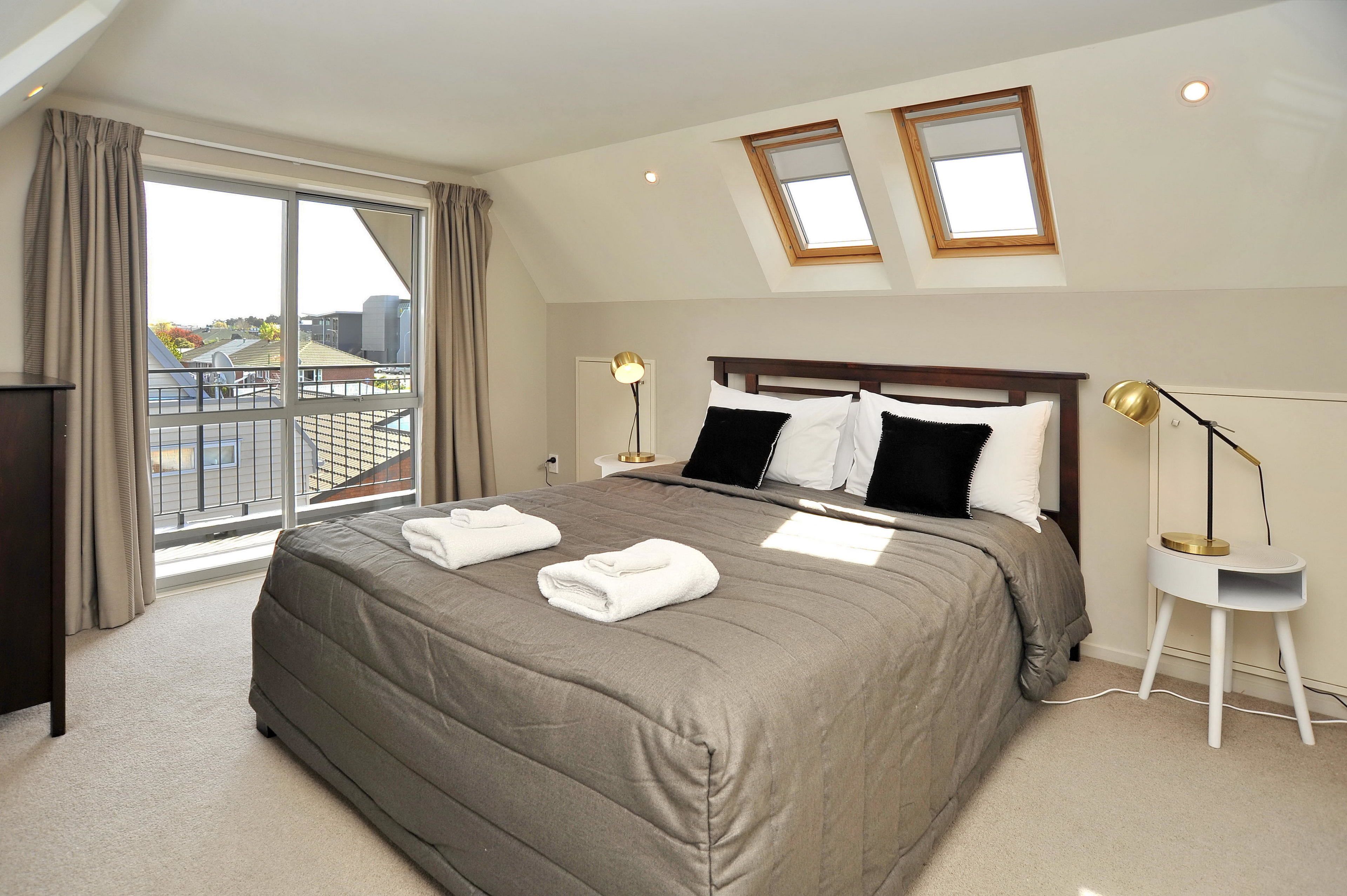 A neatly made bed with towels, a bedside lamp, and a view of the outside through a large window.
