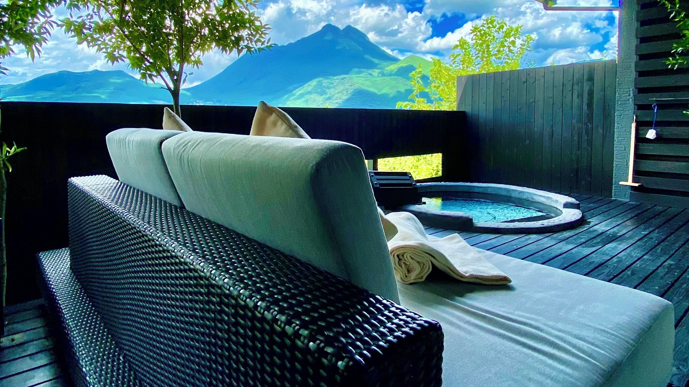 A wicker sofa with cushions, a small hot tub, and a view of mountains.