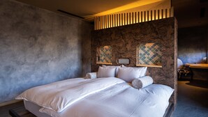 Un grand lit recouvert de draps blancs, dans une chambre moderne aux murs en pierre et au chevet en bois.