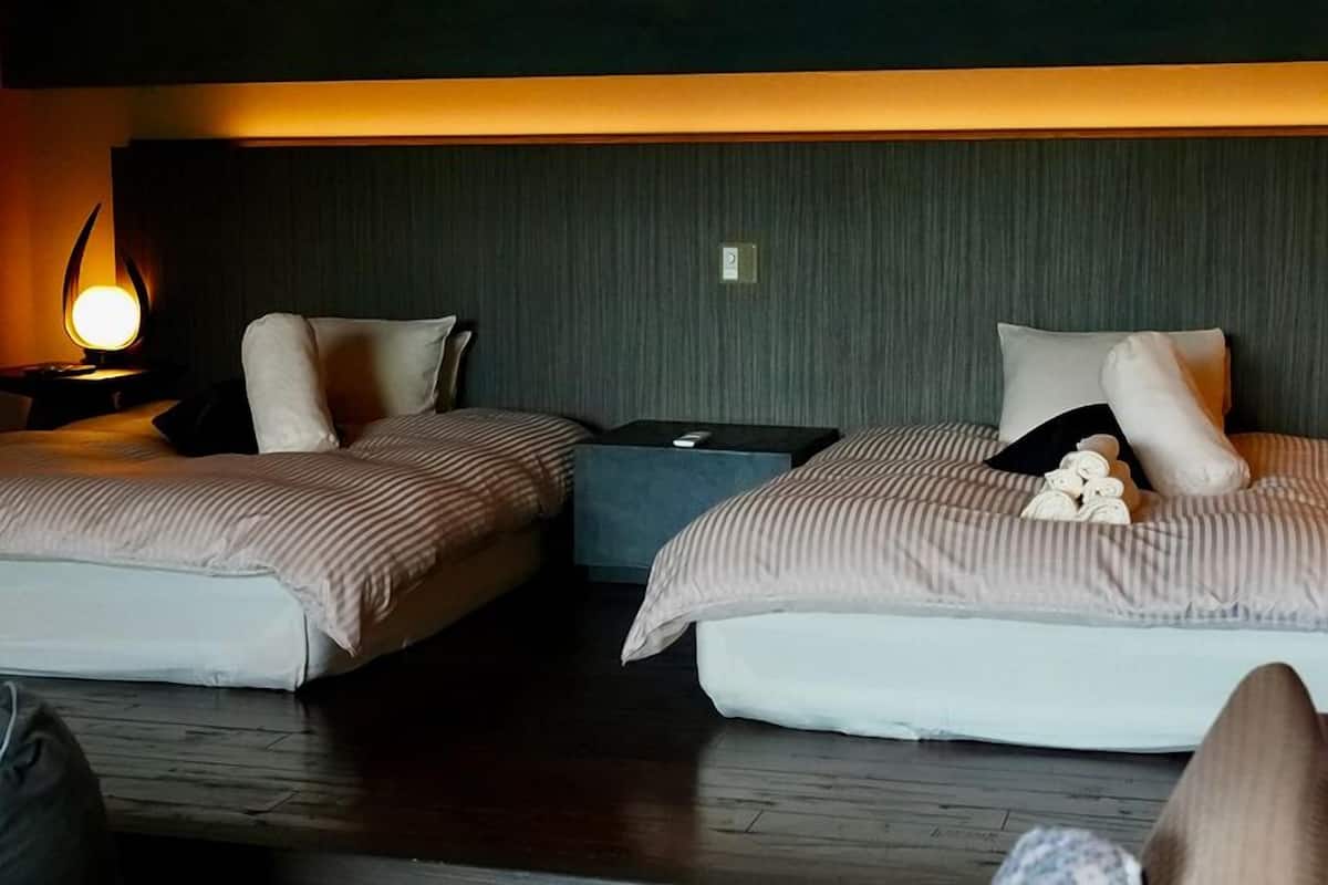 Deux lits simples avec des têtes de lit, des tables de chevet avec des lampes et une petite table d’appoint placée entre les deux.