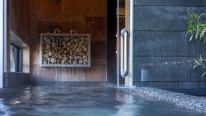 Un espace de bien-être doté d’un mur en pierre, d’un élément décoratif aquatique et d’une porte en métal.