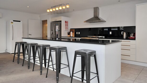 A modern kitchen with a central island, bar stools, stainless steel appliances, and a black countertop.