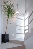 A staircase with a potted palm plant, a wall-mounted light fixture, and a large window with a view of the outside.