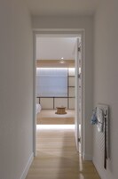 A hallway leading to a bedroom with a bed, a small wooden table, and a wall-mounted radiator.