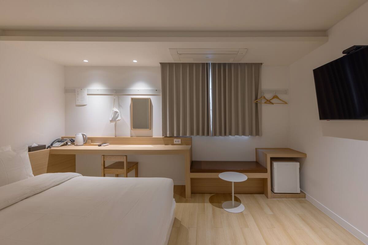 A hotel room with a bed, desk, chair, small table, and a TV.