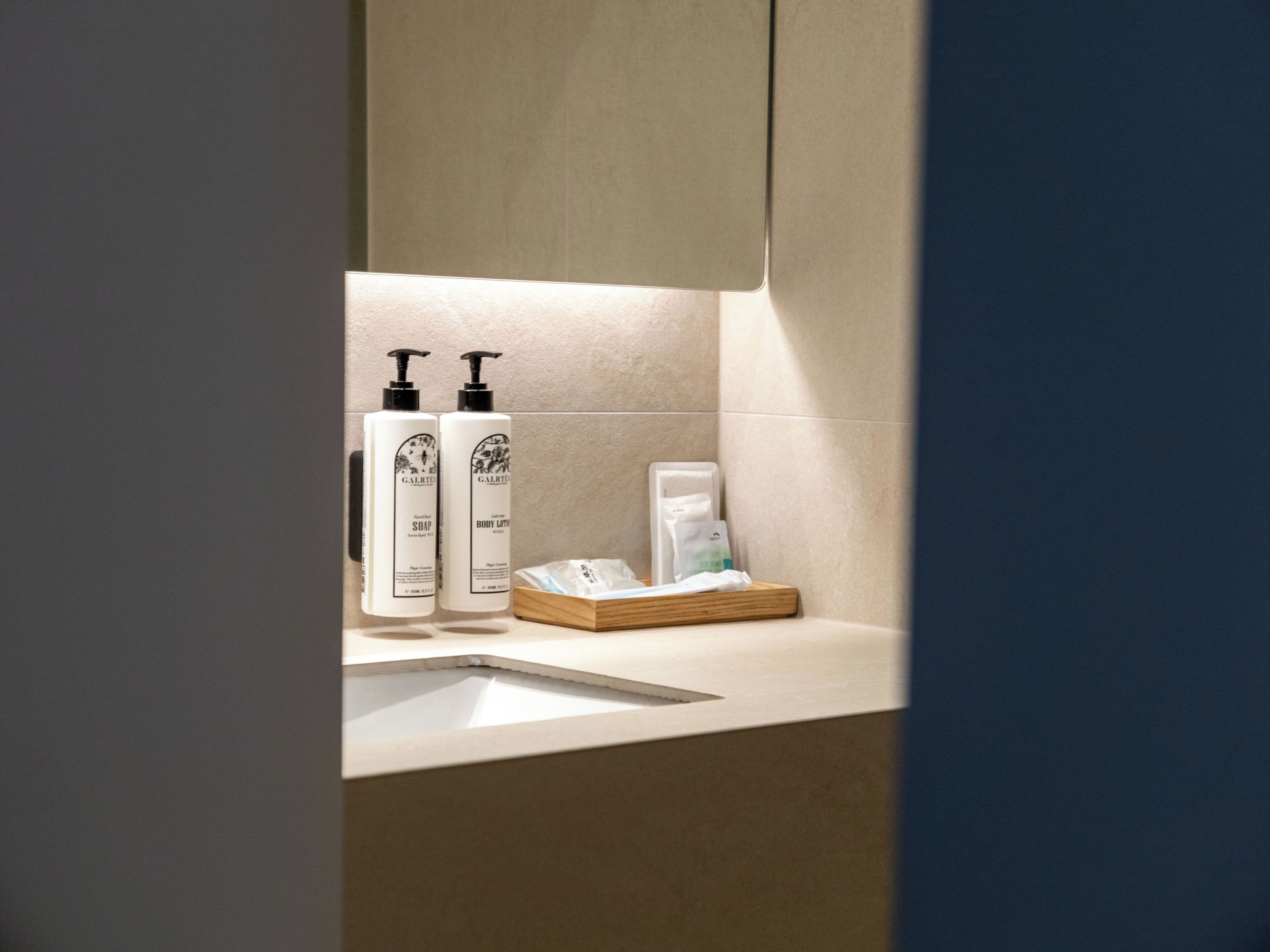 A bathroom with a sink, two soap dispensers, a tissue box, and a towel.