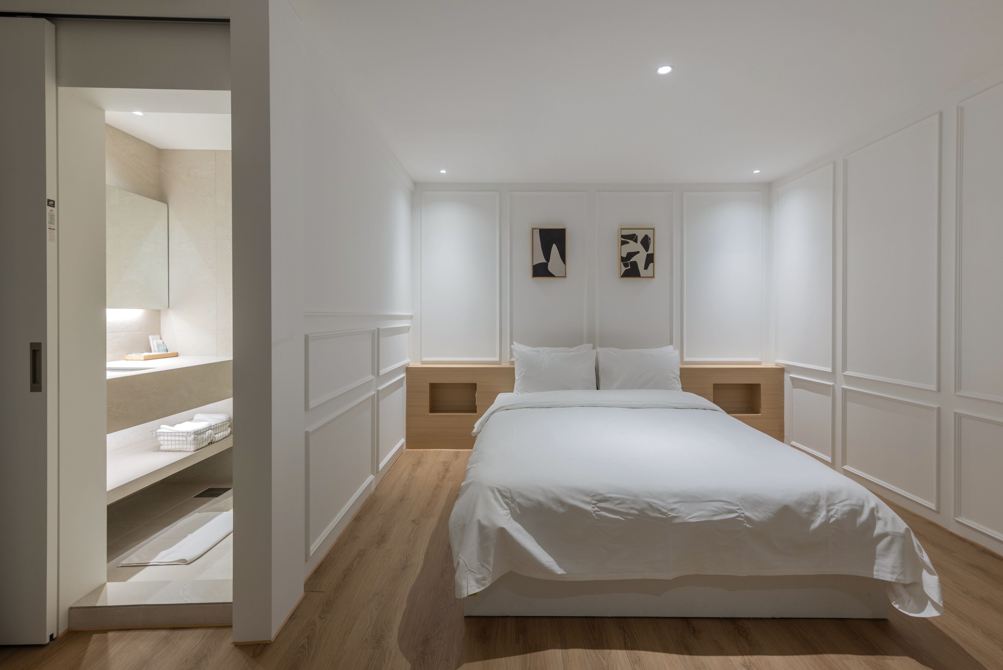 A bedroom with a bed, nightstands, a wooden floor, a built-in wardrobe, and two wall-mounted artworks.