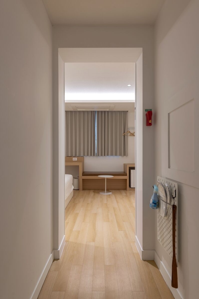 Pasillo que lleva a un dormitorio con cama, mesita de noche y perchero.