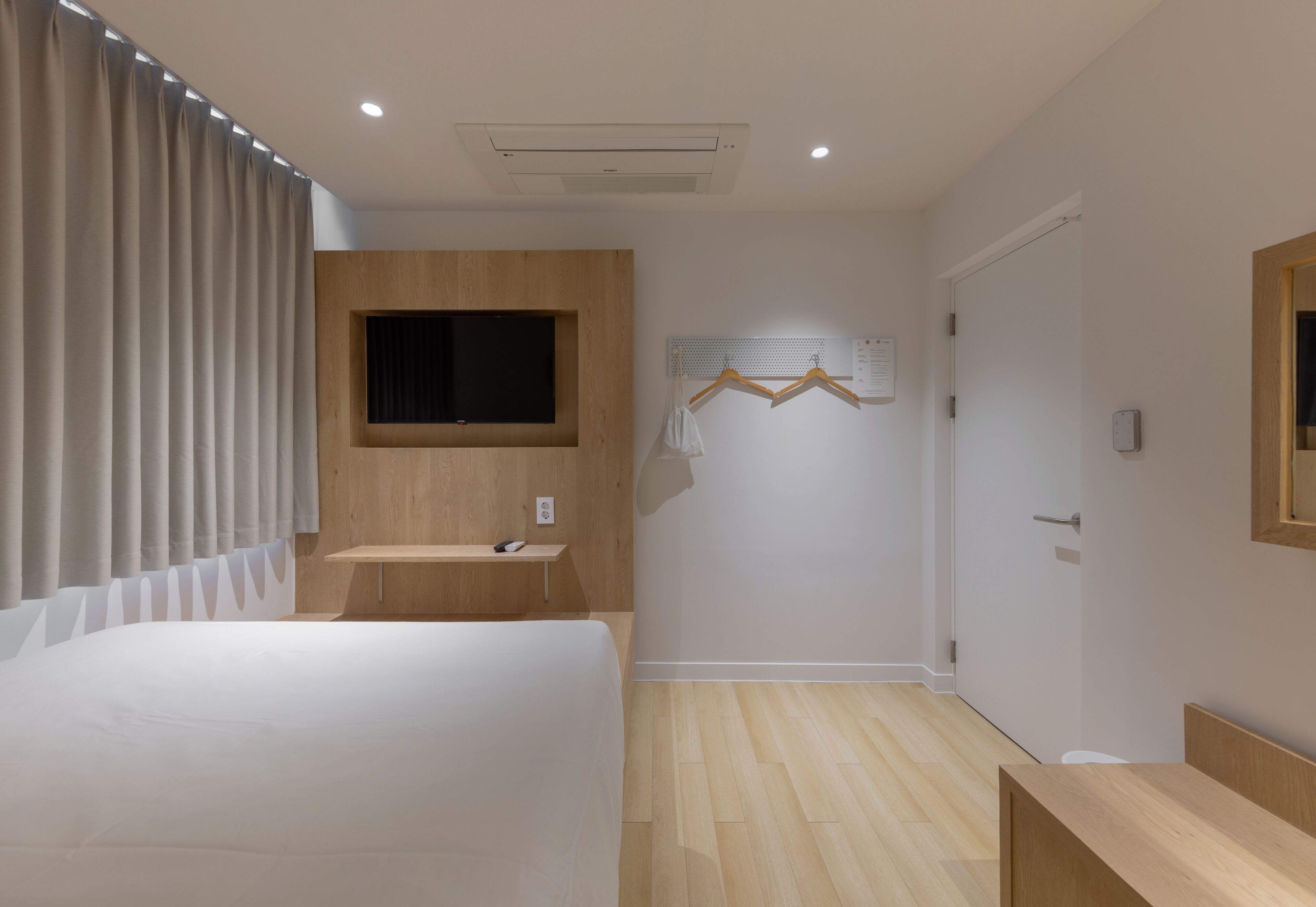 A modern bedroom with a bed, bedside table, wooden panel wall, mounted TV, and a wall-mounted drying rack.