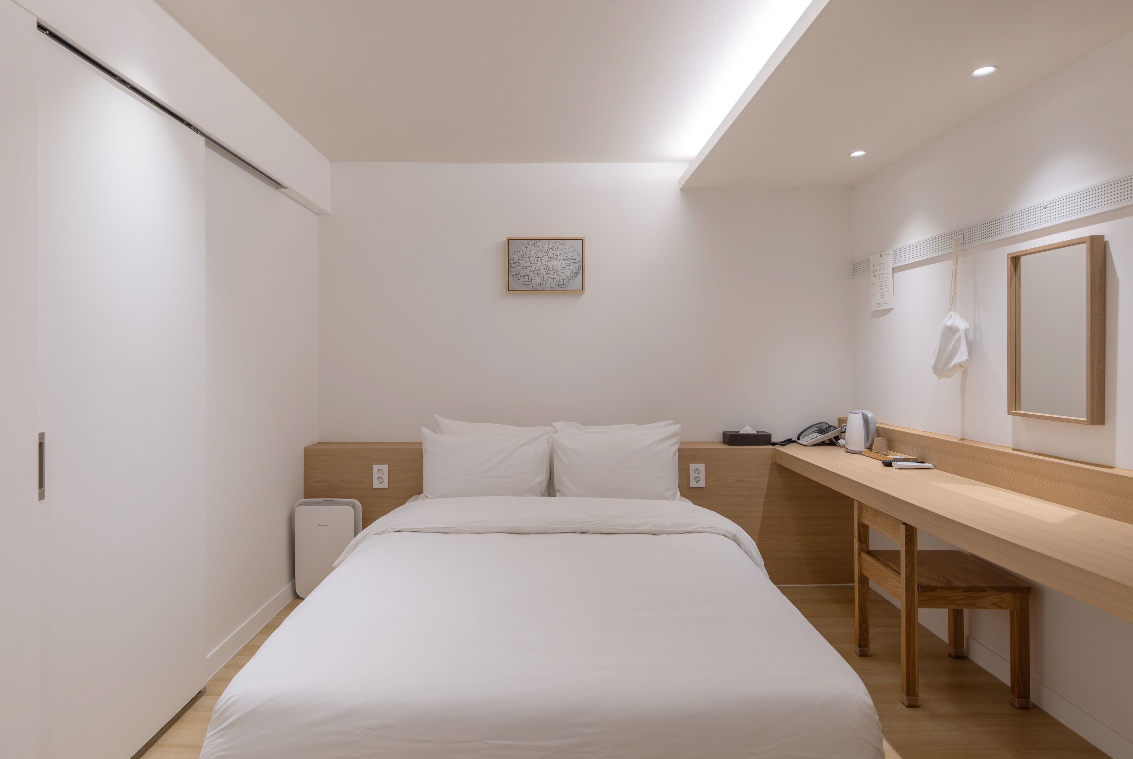 Una habitación de hotel moderna con una cama, un escritorio, un espejo y una pequeña obra de arte en la pared.