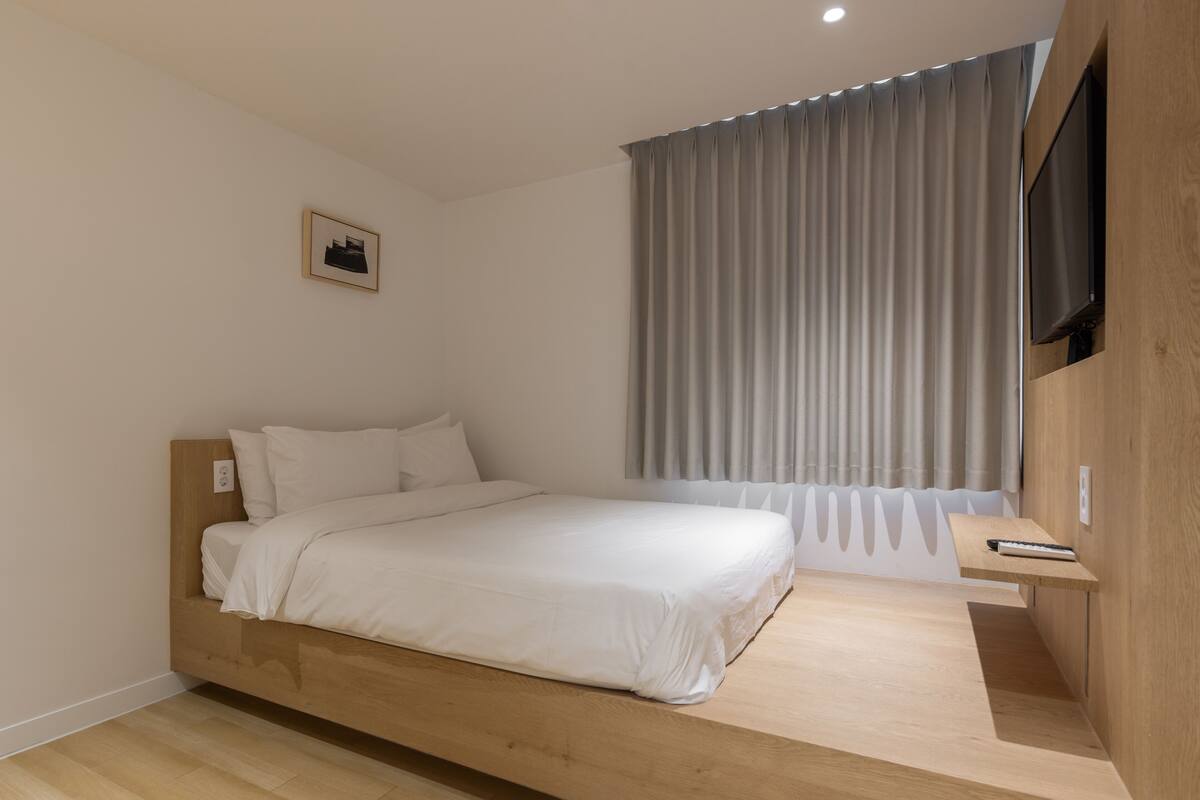 A modern bedroom with a wooden bed, a mounted TV, and a window with curtains.