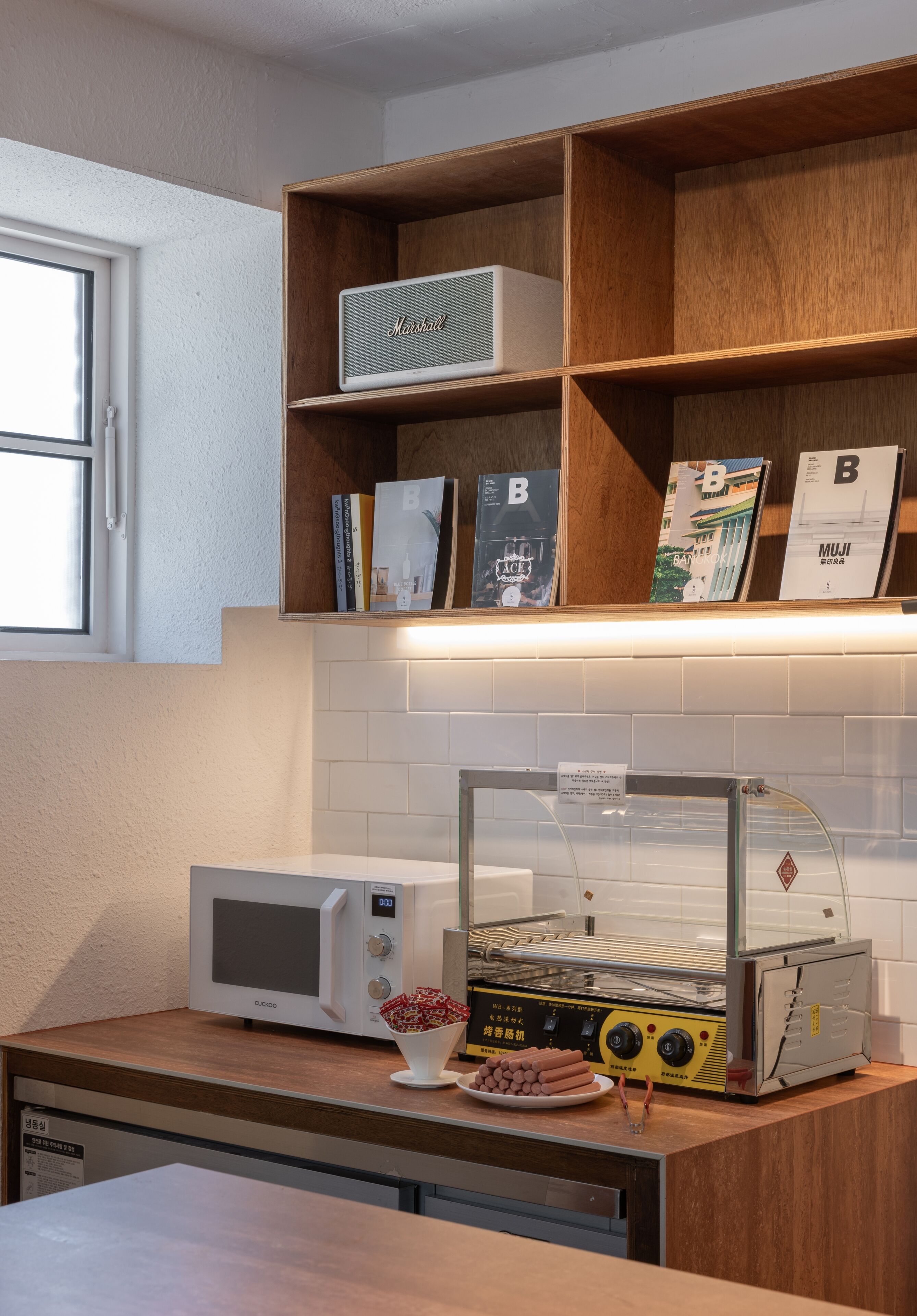 Una cocina con microondas, tostadora y una estantería con libros y un altavoz.