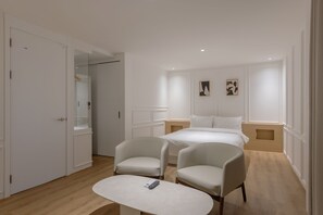 Ein modernes Hotelzimmer mit einem Bett, zwei Sesseln, einem kleinen Tisch und einem Kleiderschrank.