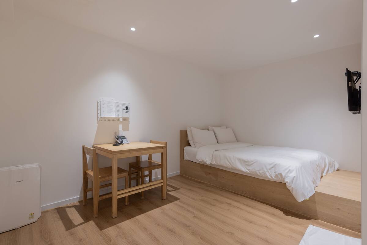A bedroom with a wooden bed, a desk with a chair, and a small radiator.