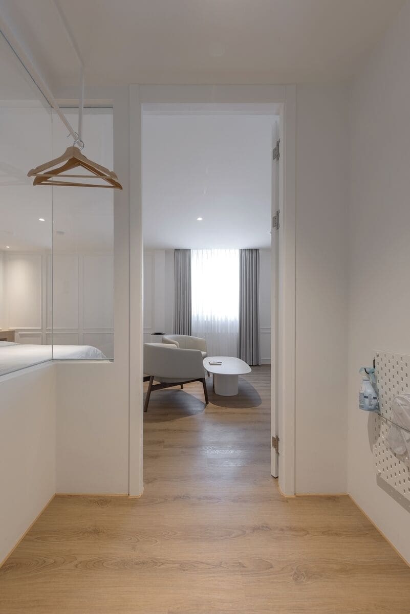A modern hotel room with a wooden floor, a bed, a desk, a chair, and a round table.