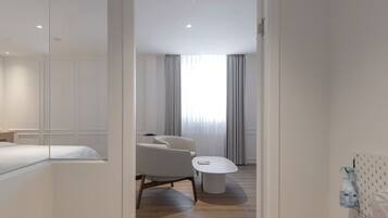 A modern hotel room with a wooden floor, a bed, a desk, a chair, and a round table.