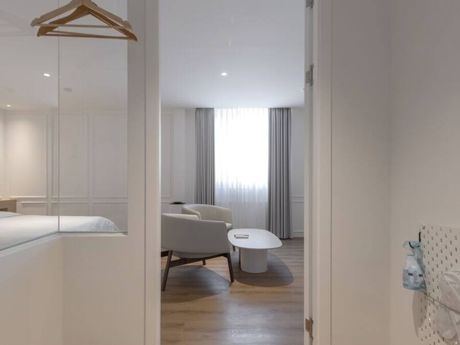 A modern hotel room with a wooden floor, a bed, a desk, a chair, and a round table.