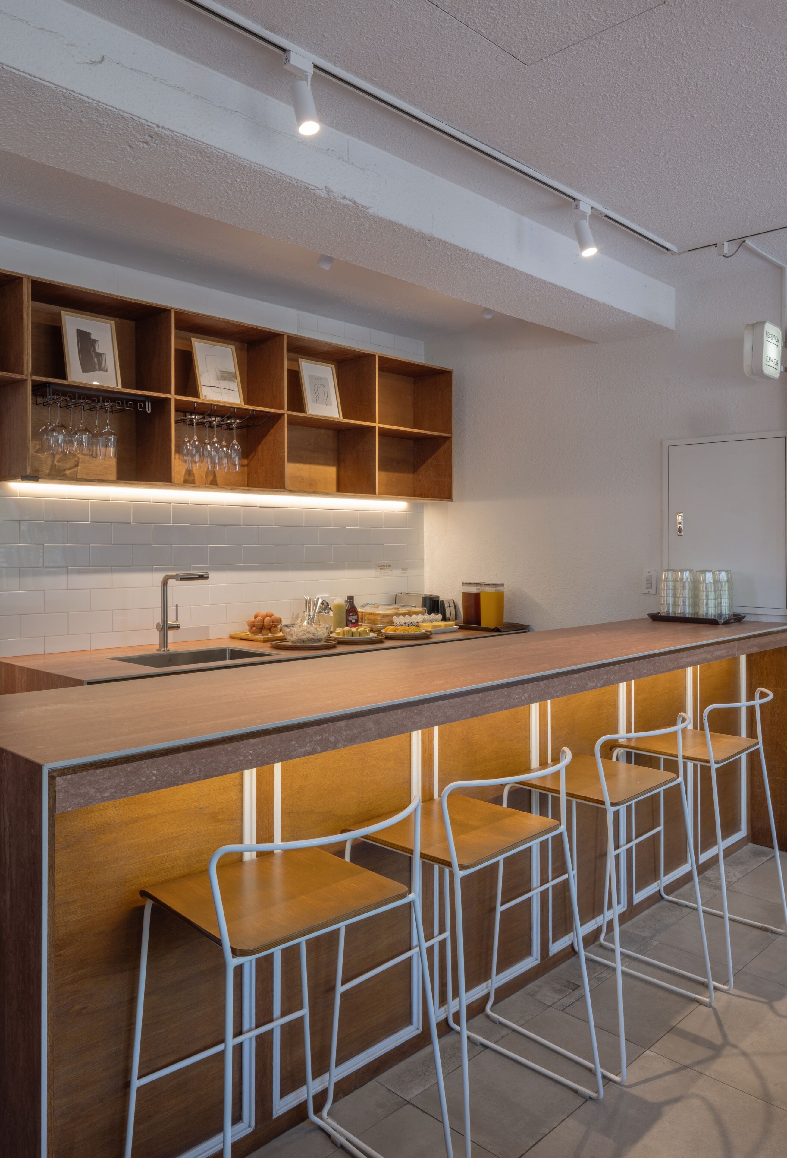 A modern kitchen with a bar area, white bar stools, and a countertop with various items.