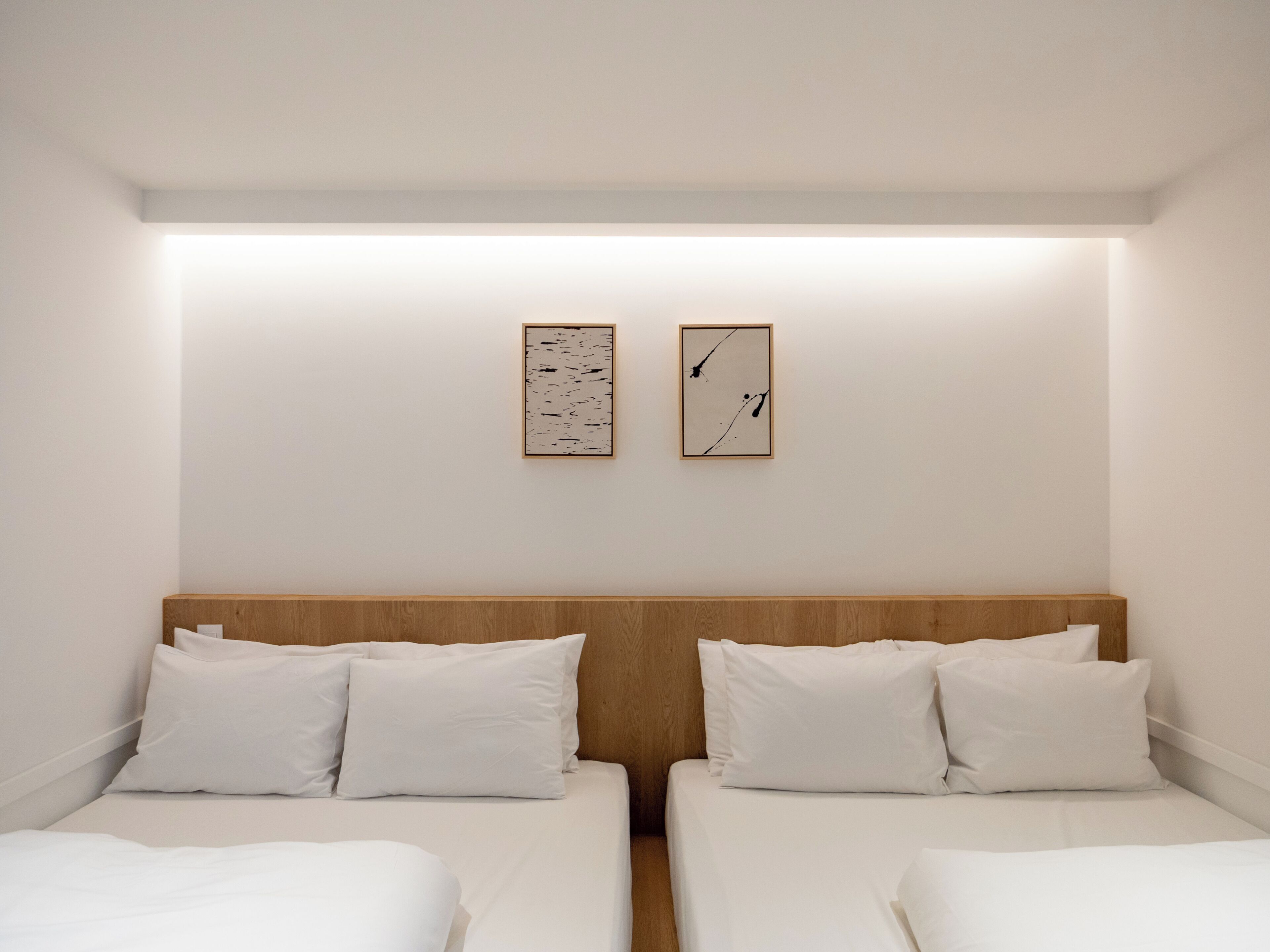 A hotel room with two single beds, a wooden headboard, white bedding, and two framed abstract artworks on the wall.