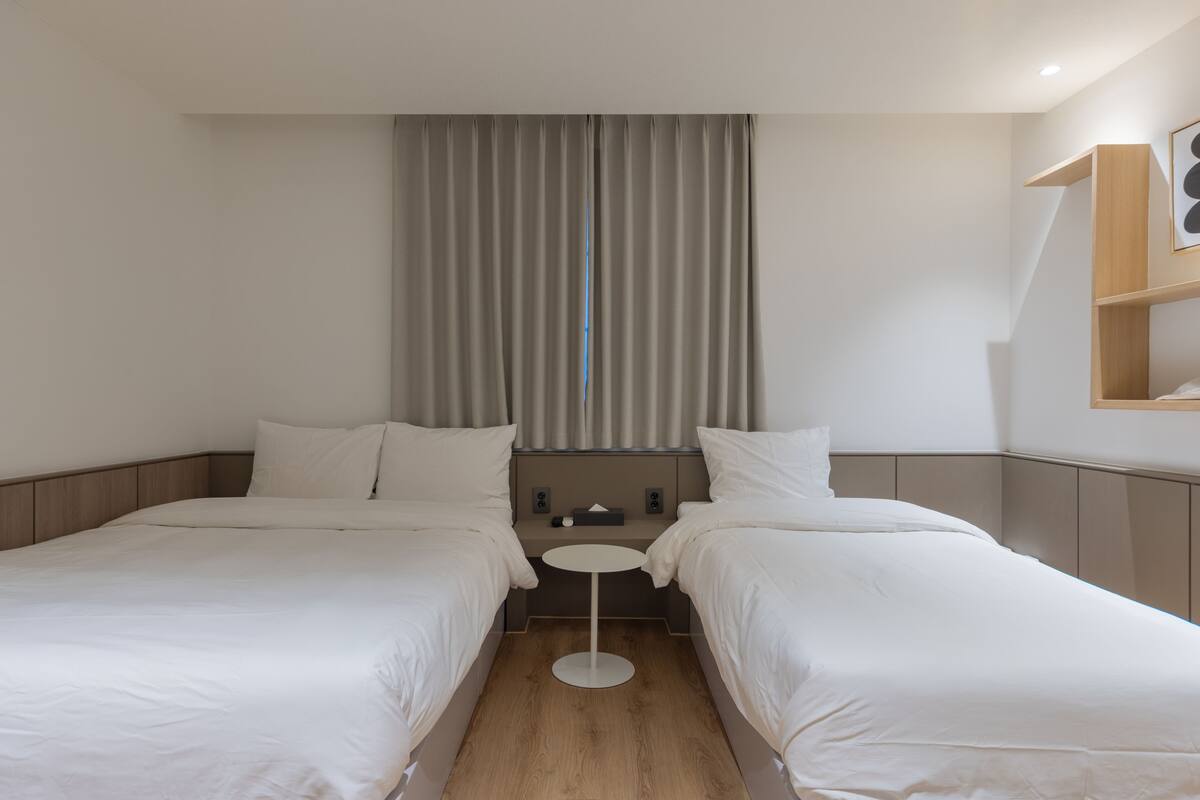 A hotel room with two beds, a small round table, a nightstand, and a window with curtains.