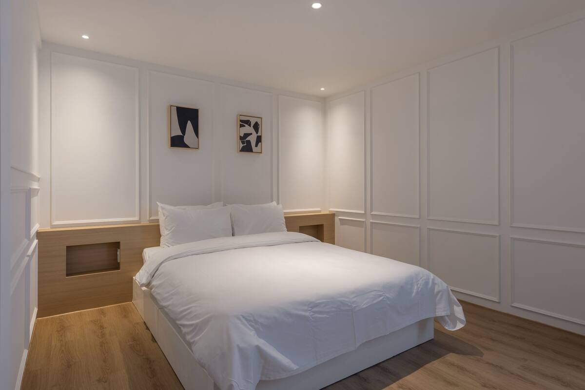 A bedroom with a large bed, wooden headboard, white walls, and recessed ceiling lighting.