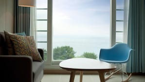 A room with a large window, a sofa, a table, and a blue chair. - The Marine Pool Villa (Gyeongju)