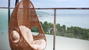 A wicker chair with a cushion, overlooking a coastal view with buildings and trees. - The Marine Pool Villa (Gyeongju)