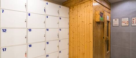 A row of numbered lockers with a wooden cabinet and a wall-mounted information board.
