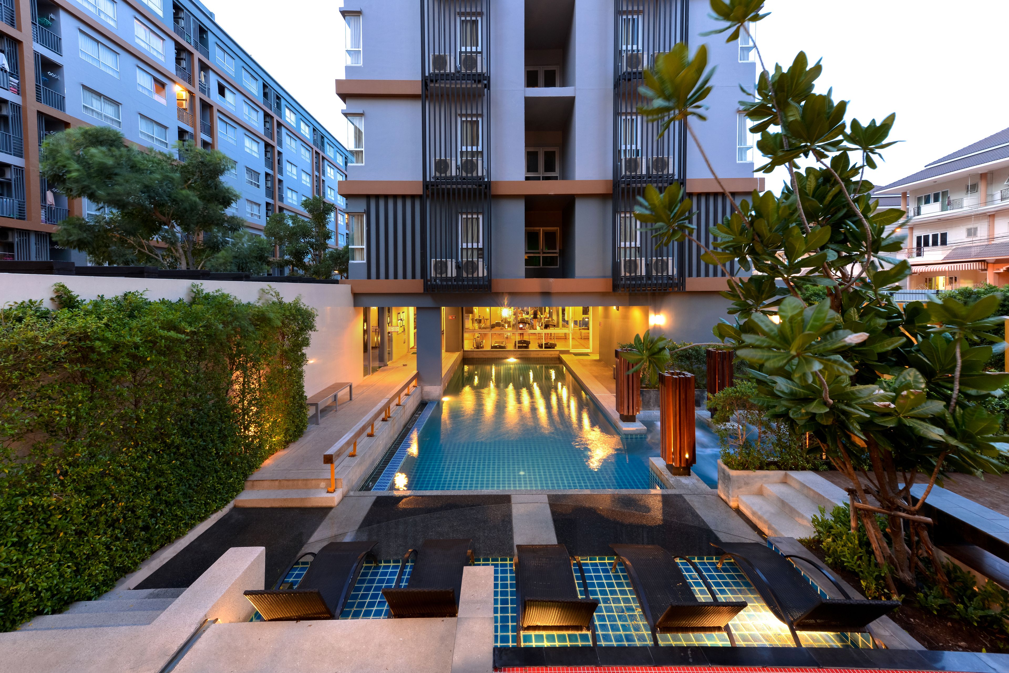 Un hotel moderno con piscina, mobiliario exterior y un jardín bien cuidado.