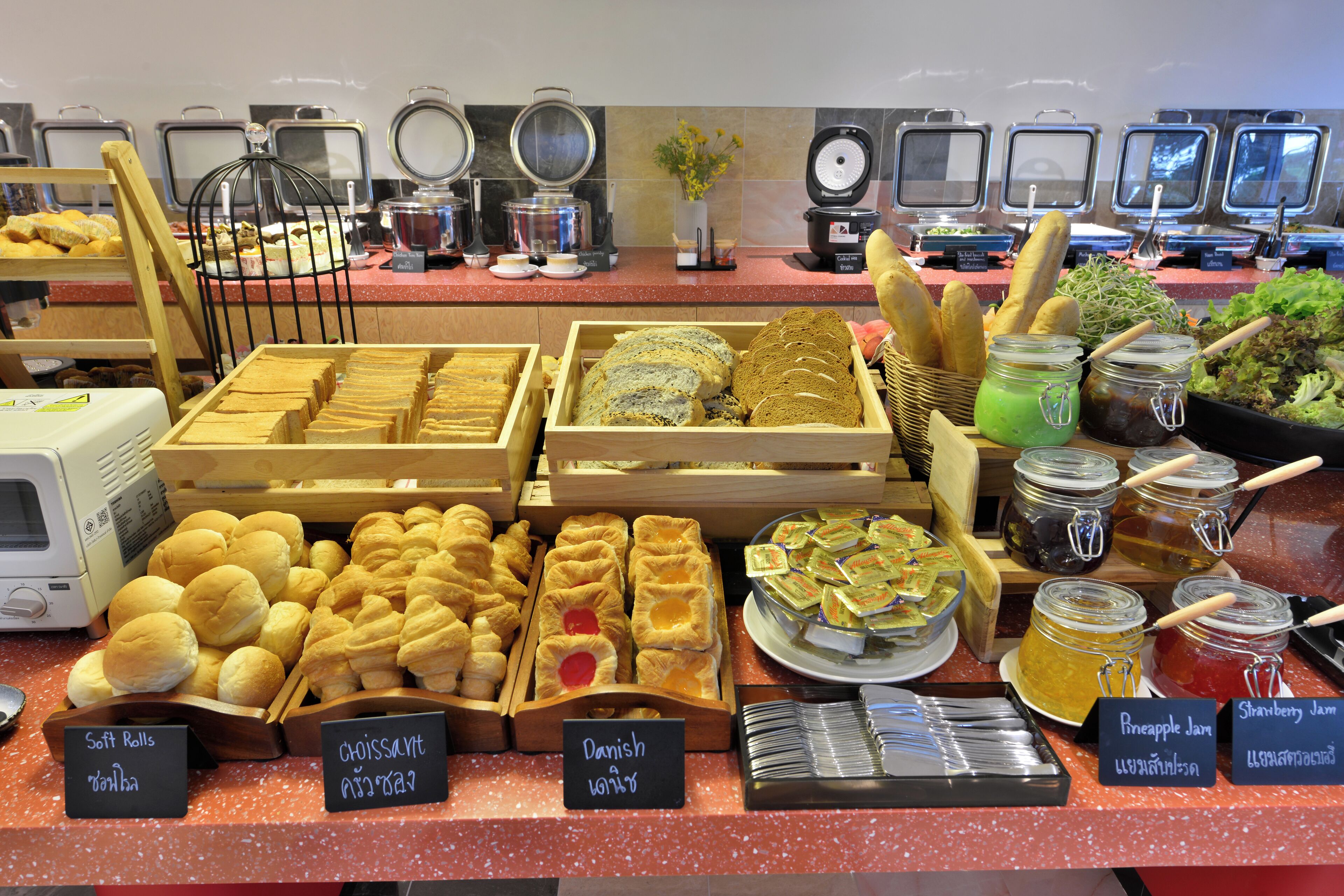 A buffet with various food items including soft rolls, Danish, and jams.