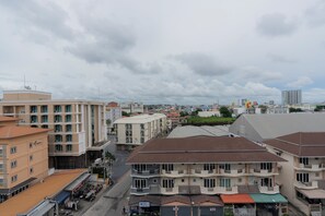 A multi-story hotel with balconies, a rooftop terrace, and a view of the cityscape. - The Grass Serviced Suites by At Mind (Pattaya)