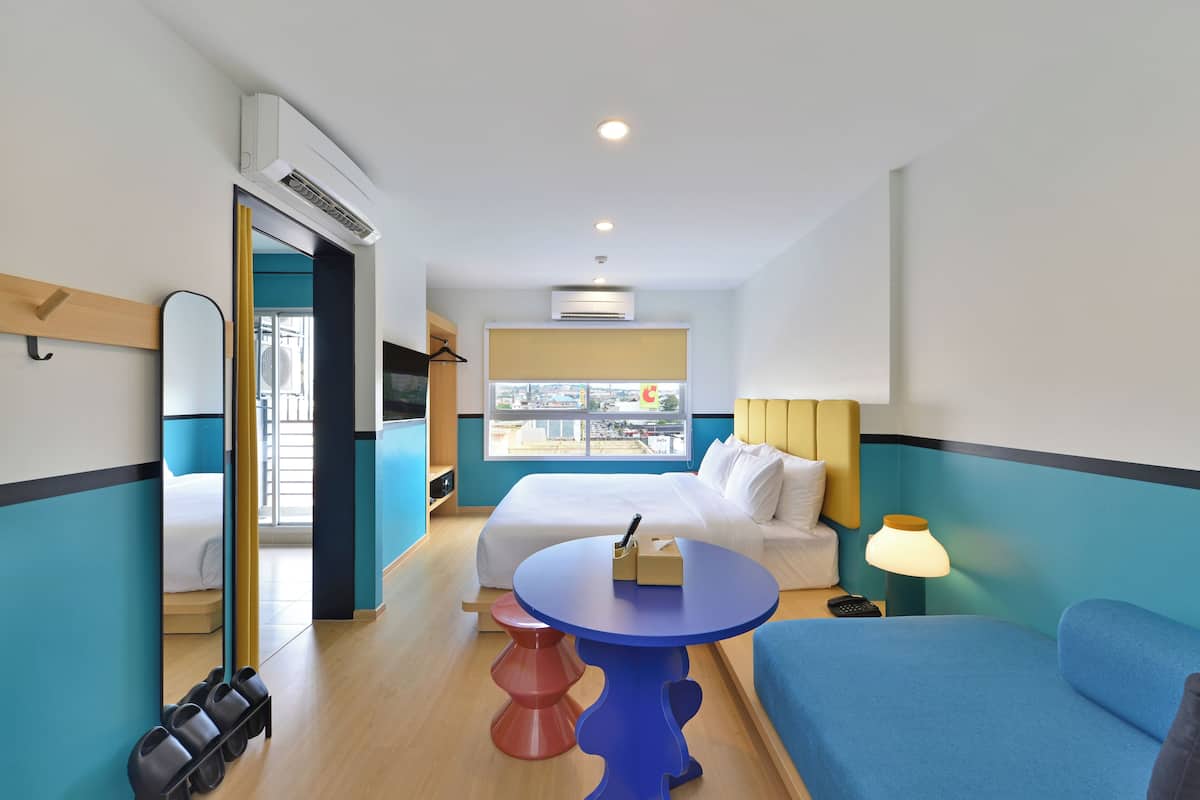 Quarto de hotel com cama, mesa redonda, luminária, espelho e janela com vista para a cidade.