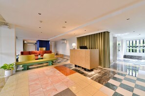 A hotel lobby with a checkered floor, a reception desk, a sofa, and a bench. - The Grass Serviced Suites by At Mind (Pattaya)