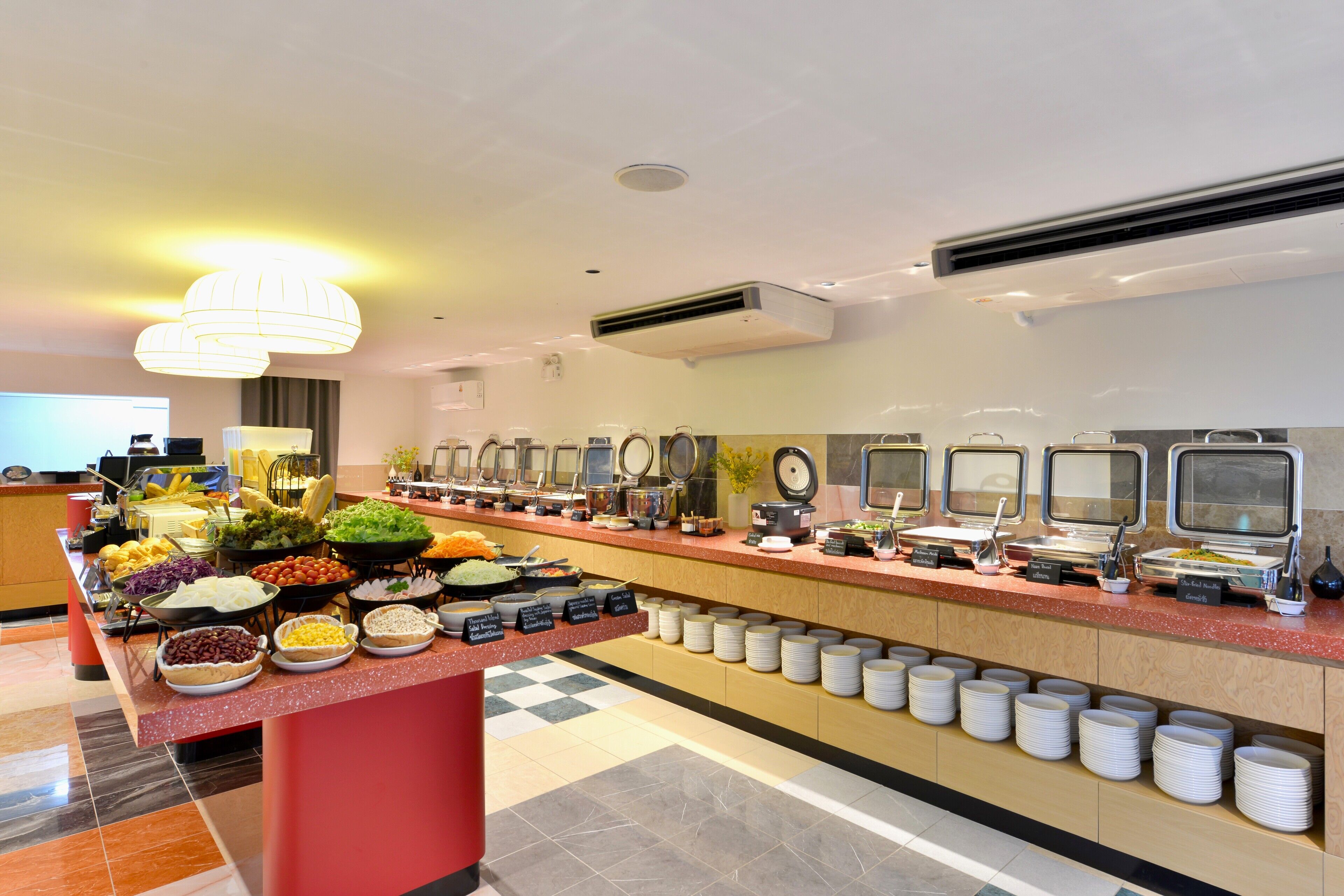 A buffet area with various food stations, including salads, fruits, and beverages, arranged on a long counter with plates and bowls.