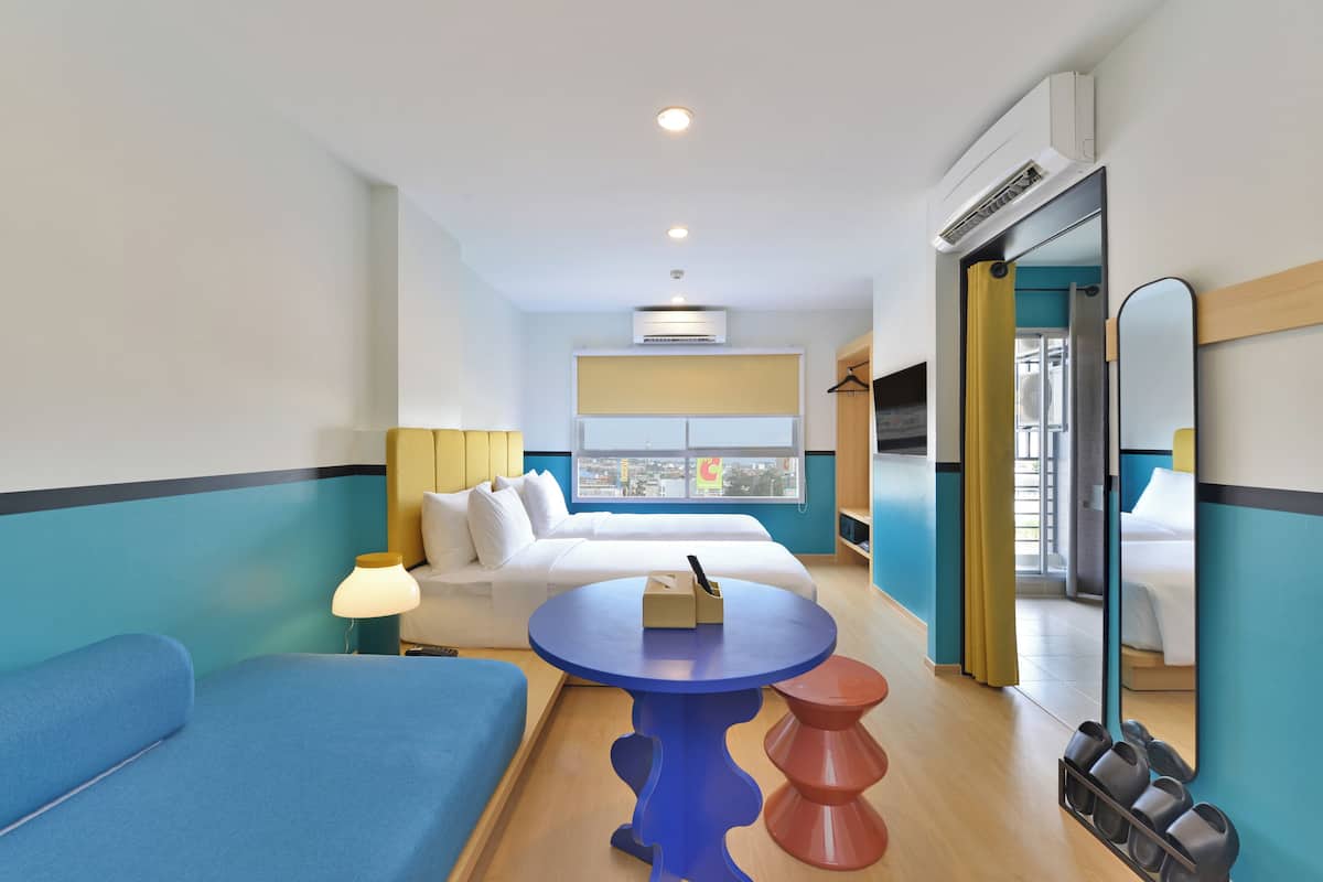 Quarto de hotel com cama, sofá azul, mesa pequena, espelho e sapateira.