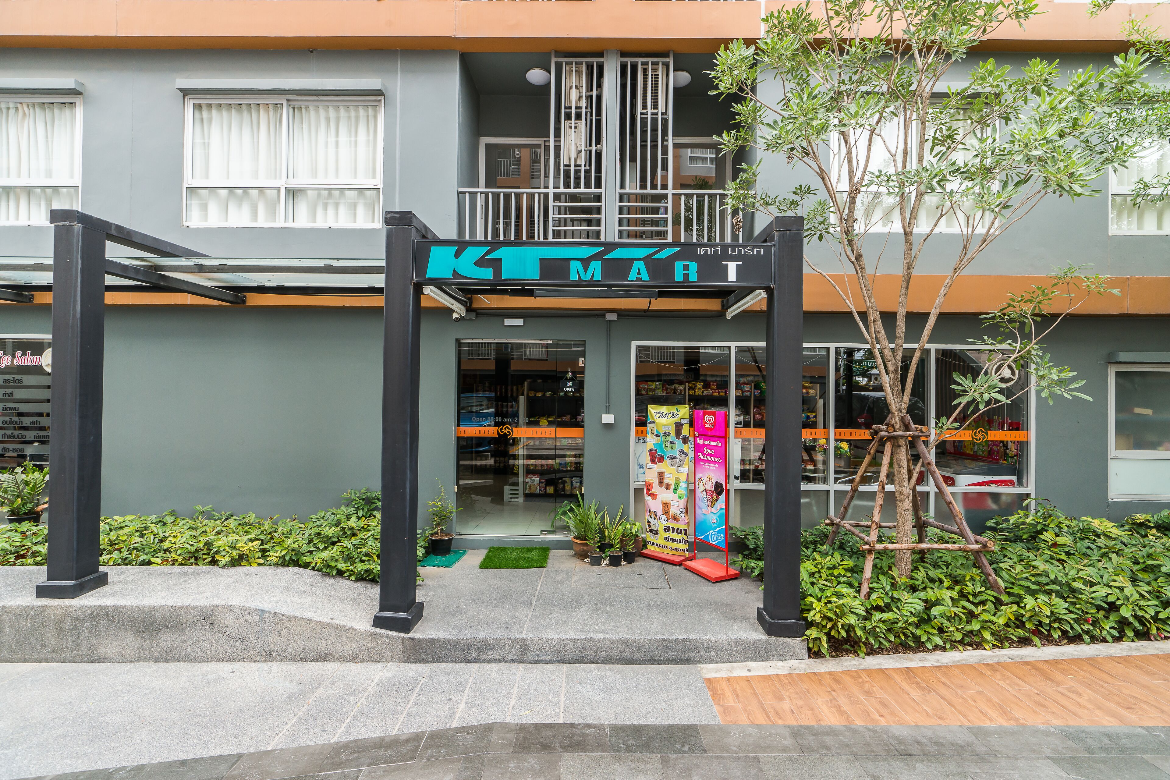 A KTMART store entrance with a modern design, including a staircase, potted plants, and a tree.