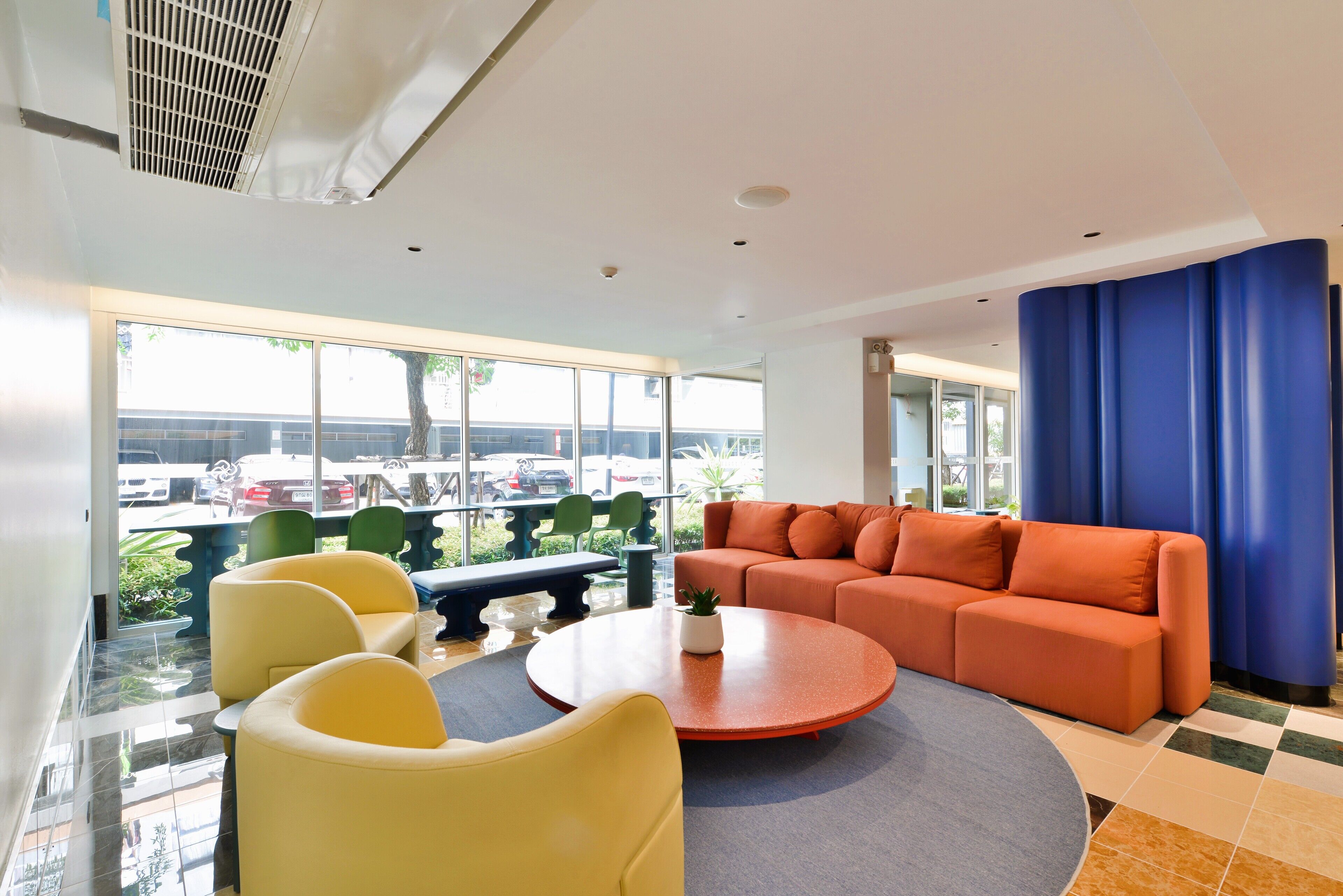 A modern hotel lobby with a large window, a sofa, yellow chairs, and a round table.