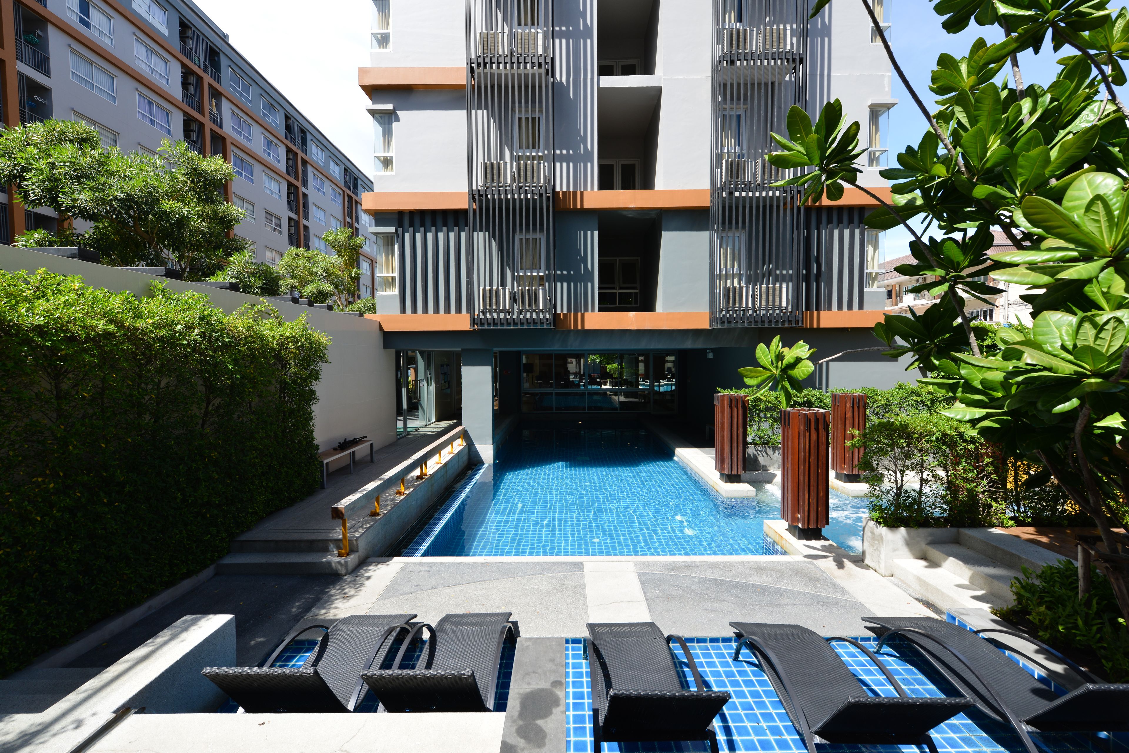 Un área de piscina con sillones de descanso, un edificio con balcones y vegetación.